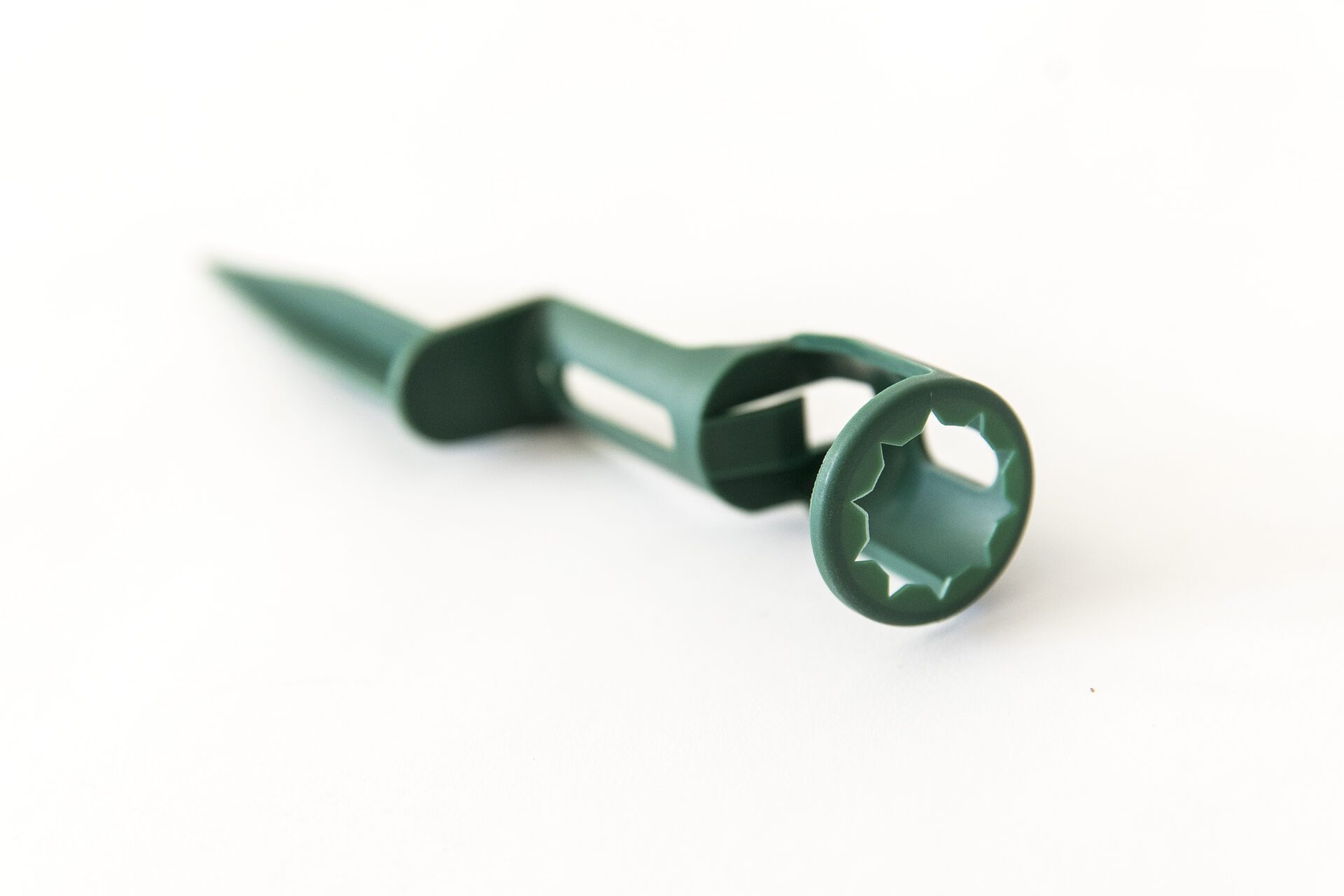 Green plastic stake with a cylindrical holder at the top and a pointed end at the bottom